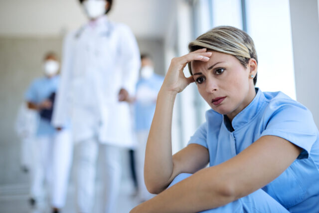 Distraught nurse sitting in a hallway and thinking of something.